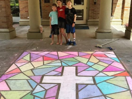 Children stand behind a chalk cross, which is set against a drawing of a stained-glass window outside of the governor's mansion in Arkansas.