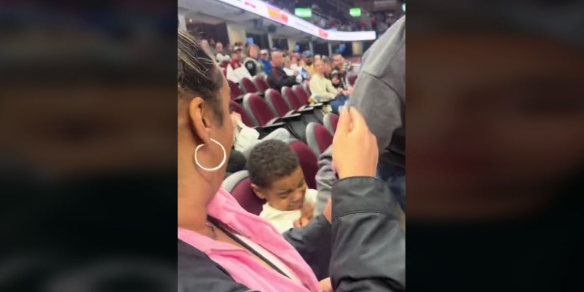 a mother looking on as a man sitting next to her son at a hockey game intercepts a puck that might have hit him